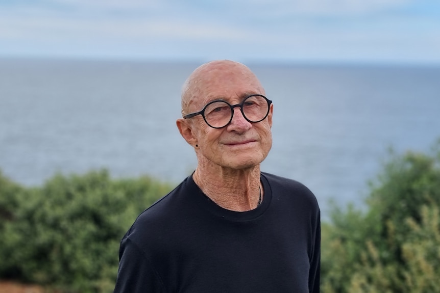 Man wearing a black shirt and glasses, with the sea in the background. 