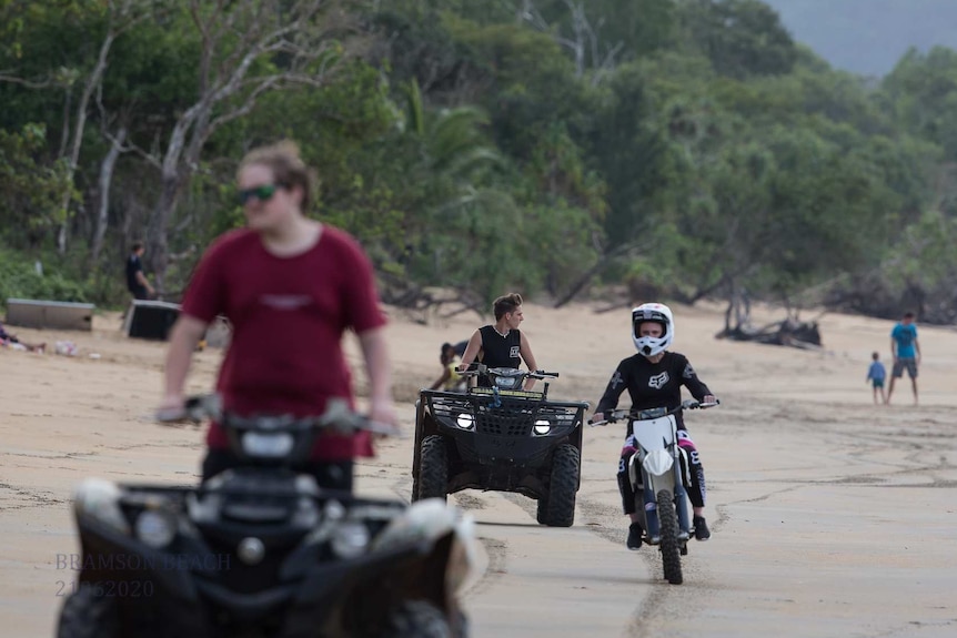 Some young men on quad bikes and a motorbike riding on a beach