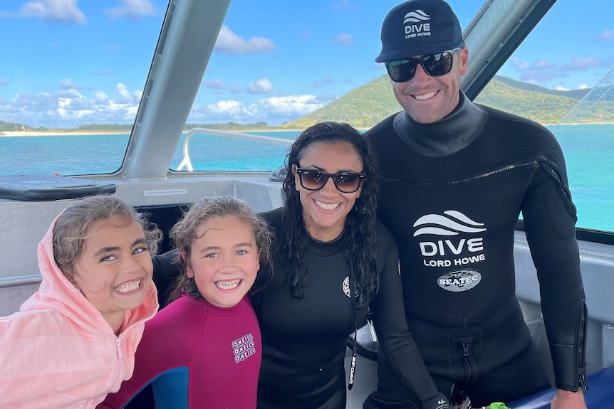 A man and woman on a boat wearing wetsuits, next tot heir two young daughters.