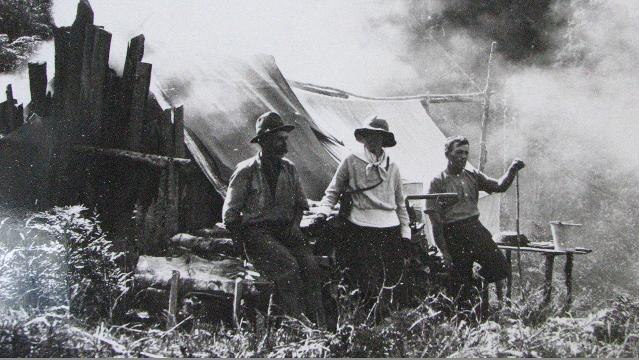 Old photograph of men sitting in front of wooden shack