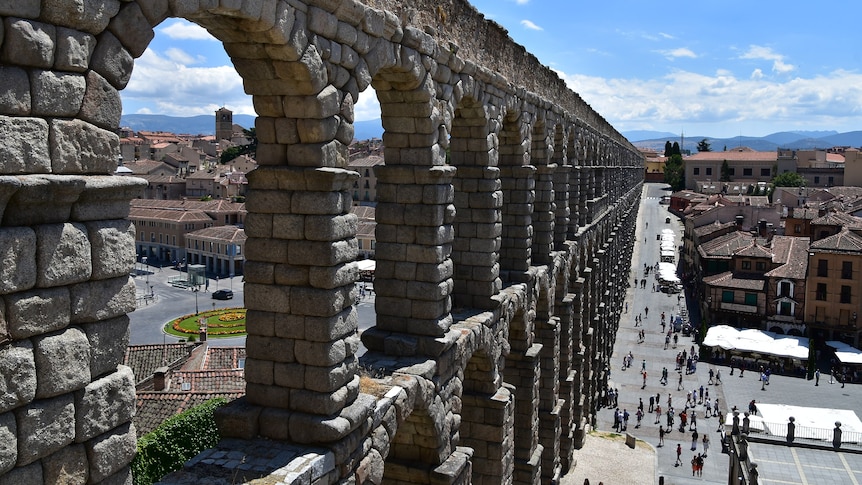 You view a soaring Roman aqueduct over a classical Spanish town.