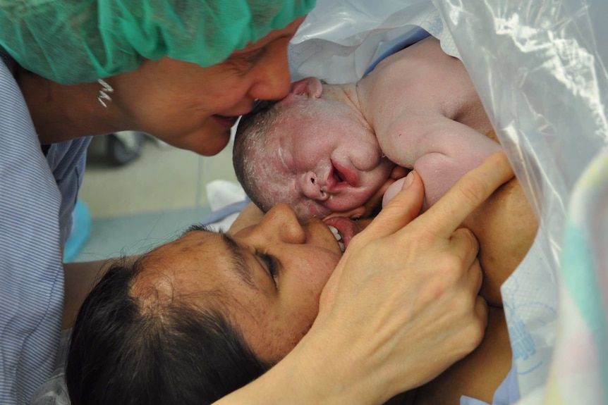 Brand new baby on chest of mother while baby's other mother looks on.