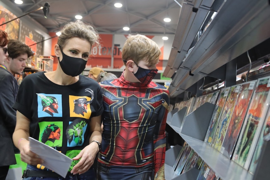 A woman and a boy in a Spider-Man costume looking at comics.