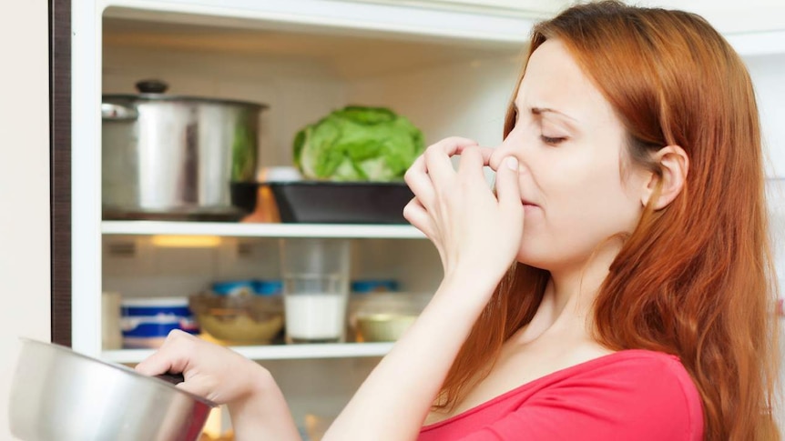 Woman smells milk in front of a fridge.