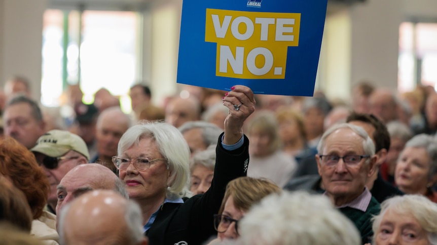 An elderly woman holds up a small poster that reads 'vote no', as part of a rally for the Indigenous Voice to Parliament.