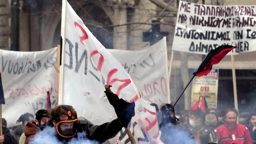 A protester kicks away a tear gas canister during clashes with riot police in central Athens