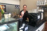 woman holds up takeaway coffee cup at cafe