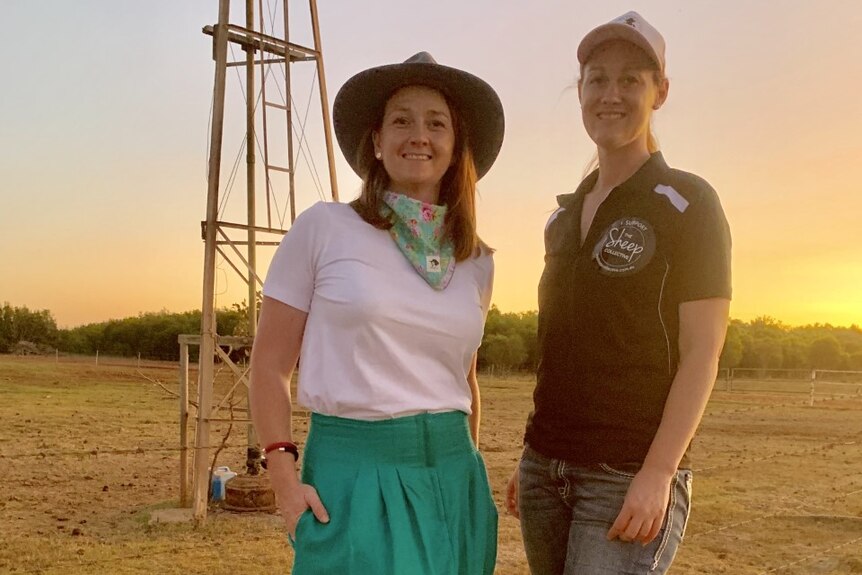 Two ladies stand in front of windmill while the sun sets