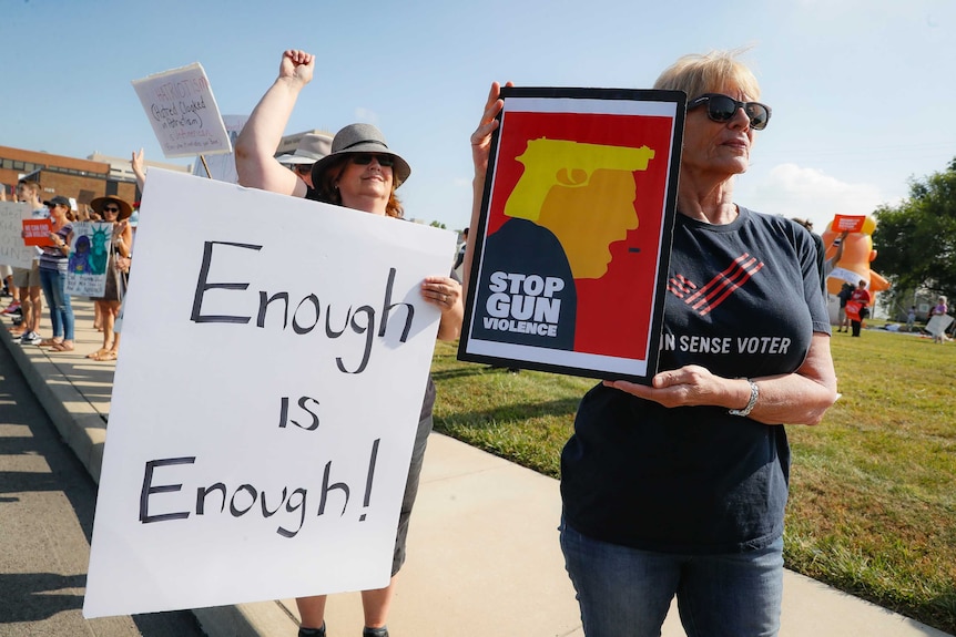 A group of protestors raise their fists in the air on a clear day and hold placards denouncing gun violence.