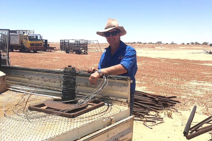 Grazier Chook Kath leans on a ute in a dusty paddock on his property.