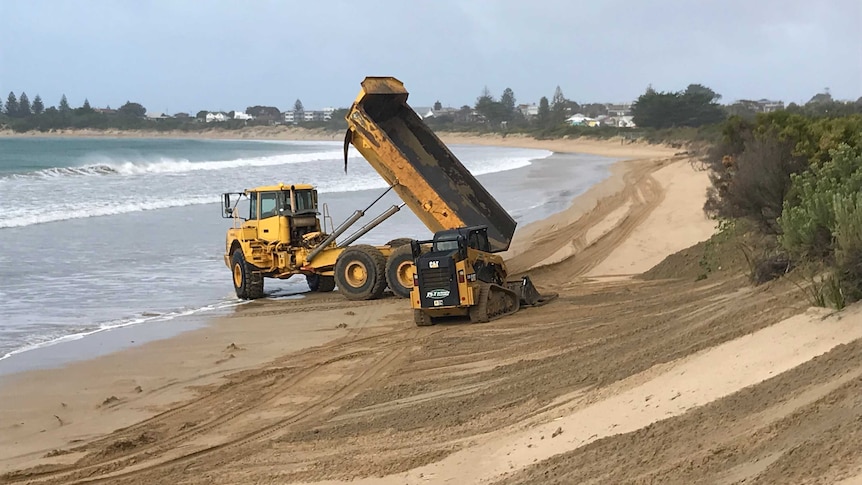 A large dump truck dumping sand on the beach along the Great Ocean Road.