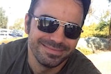 A man with dark hair and sunglasses.