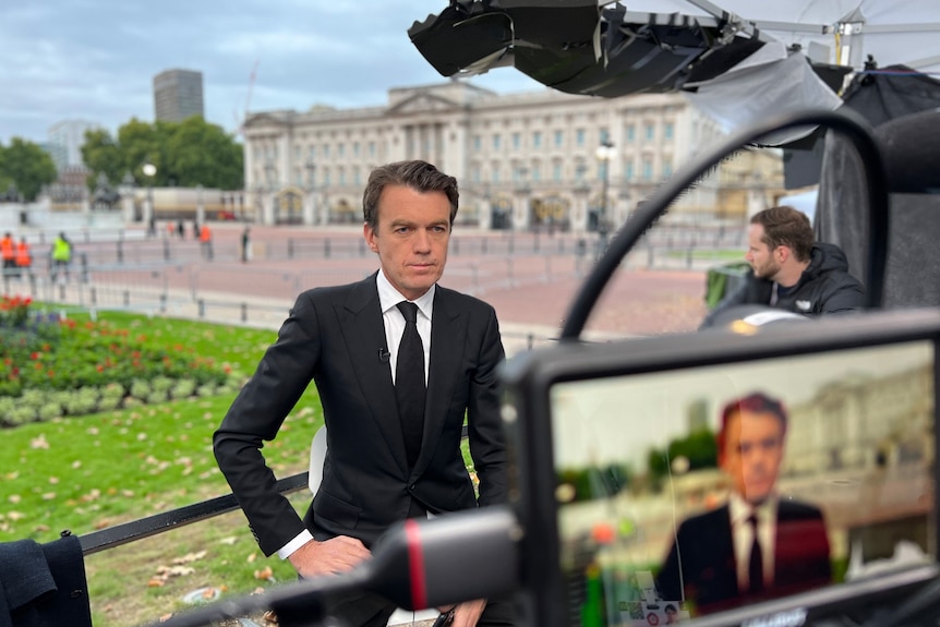 Camera filming Michael Rowland with Buckingham Palace in the background.
