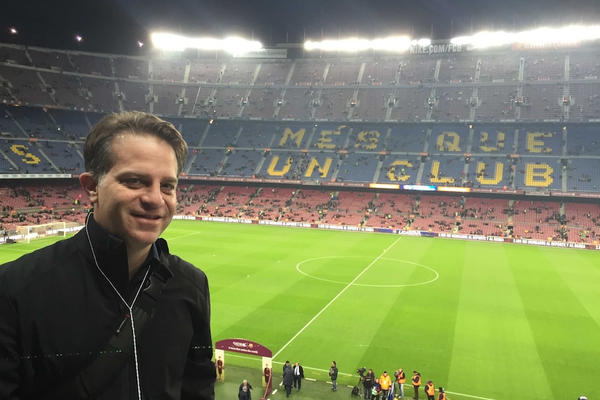 Sam Walker stands in the stands in a large sporting arena.