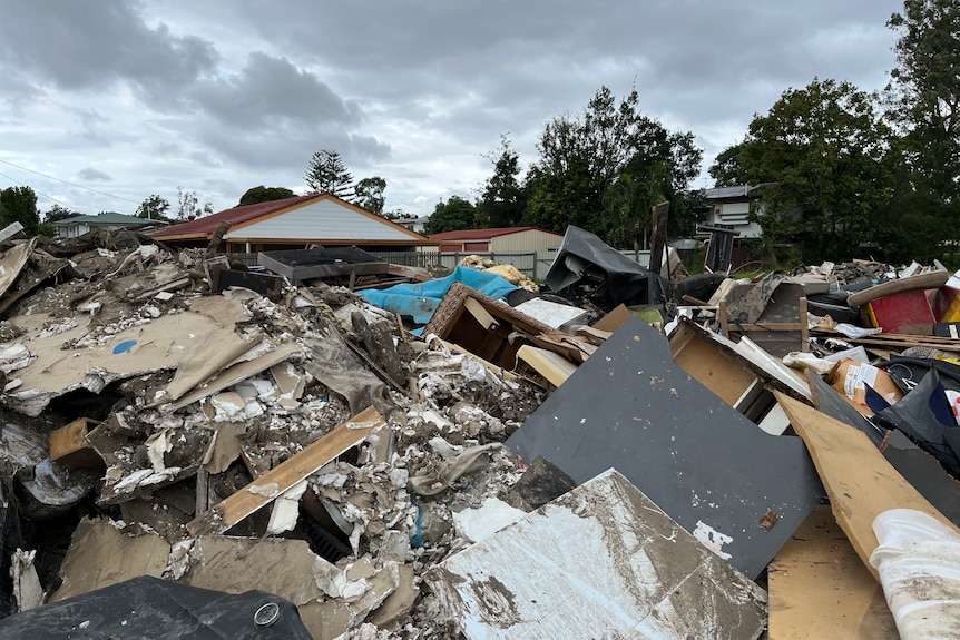 An image of flood waste piling up at a park with houses nearby. 