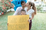 Couple kissing in front of pregnancy announcement