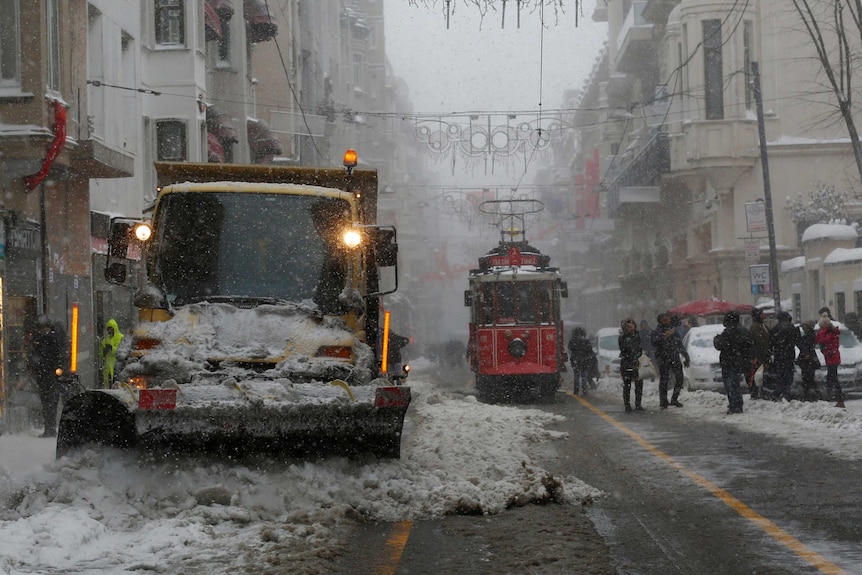 A snow cutter cleans dirty snow from a pedestrian street as tram approaches