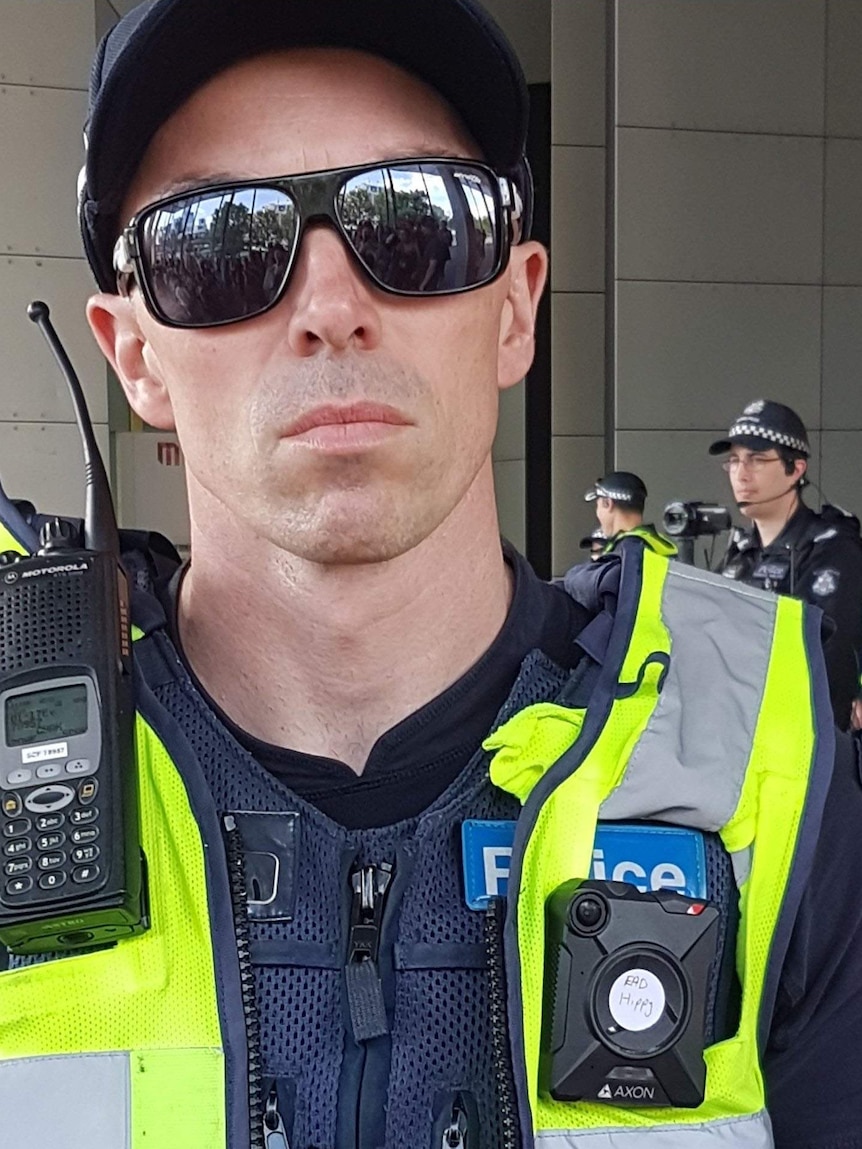 A Victoria Police officer wearing sunglasses and a sticker on his body cam which says EAD hippy.