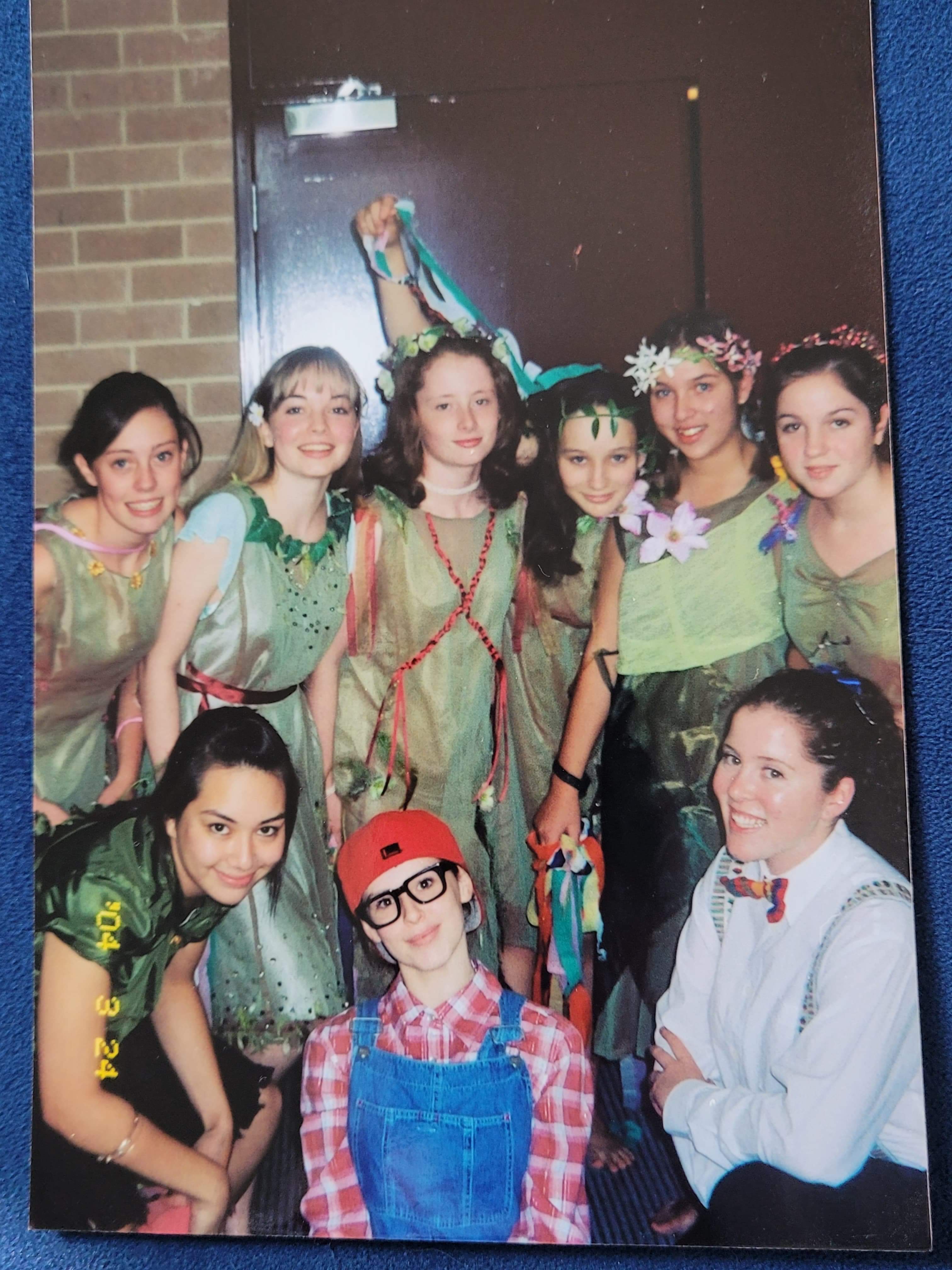 A group of teenaged girls dressed in fairy costumes, with Laura Murphy in the centre, dressed in blue overalls.