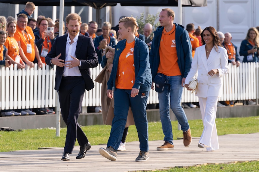 Prince Harry and Meghan Markle, Duchess of Sussex, arrive at the Invictus Games venue with people watching behind a white fence