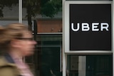 The blurred image of a woman walking past an office building with an 'Uber' sign prominently displayed.