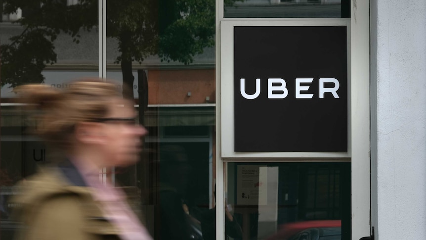 The blurred image of a woman walking past an office building with an 'Uber' sign prominently displayed.