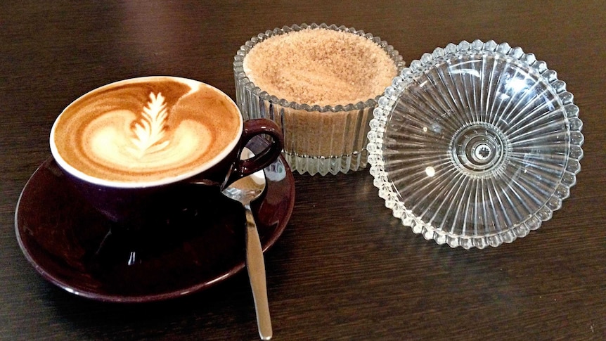 A cup of coffee with sugar sitting on a table.