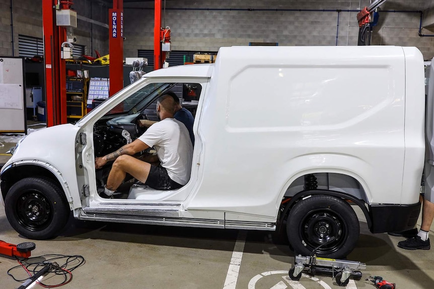 Workers sit in two-seater electric van called the 'Cargo' being built in a Logan warehouse.