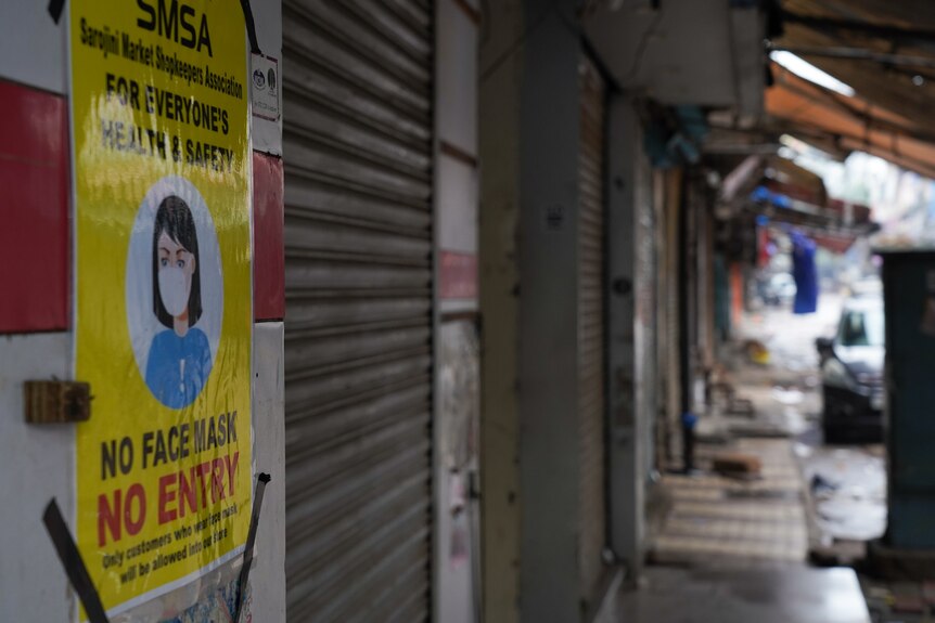 A sign displaying no face mask no entry hangs on a wall on an empty street.