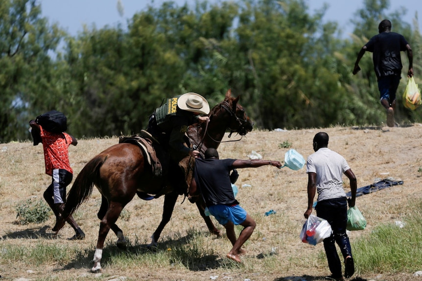 A US border patrol officer on horseback grabs the shirt of a migrant trying to return to the United States.