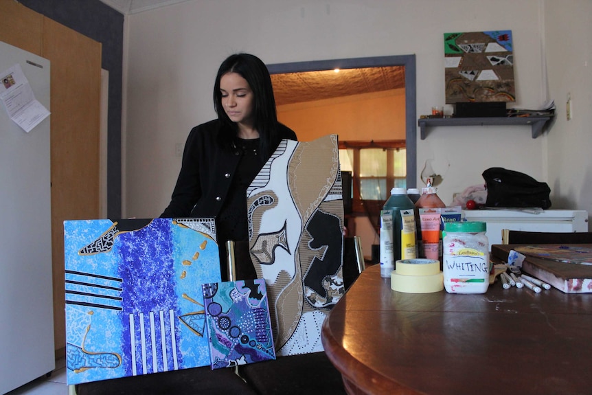 Jade Cicak stands behind three pieces of her work that are standing upright on chairs