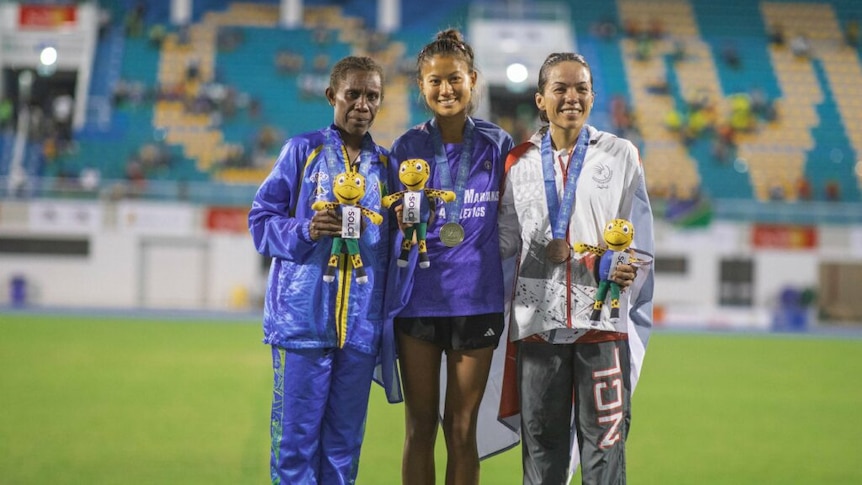 Three women stand together on a podium, smiling.