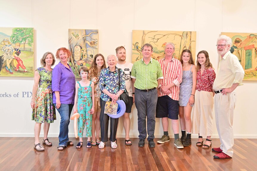 A group of 11 people, varying in ages, pose together in front of artworks at an exhibition.