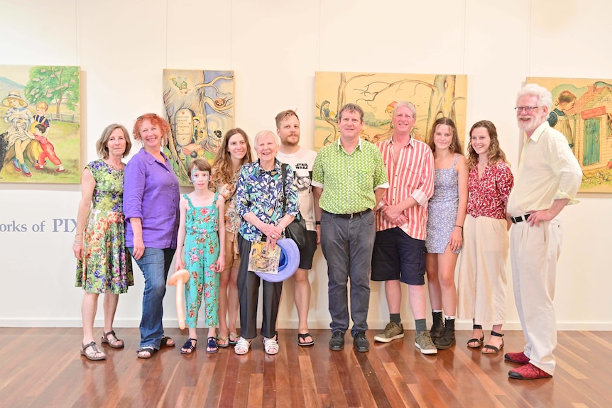 A group of 11 people, varying in ages, pose together in front of artworks at an exhibition.