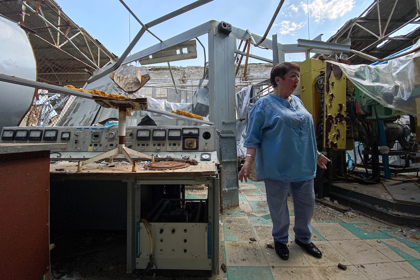 A woman is standing in a scientific department that has been heavily damaged. The roof is gone and there is debris on the floor.