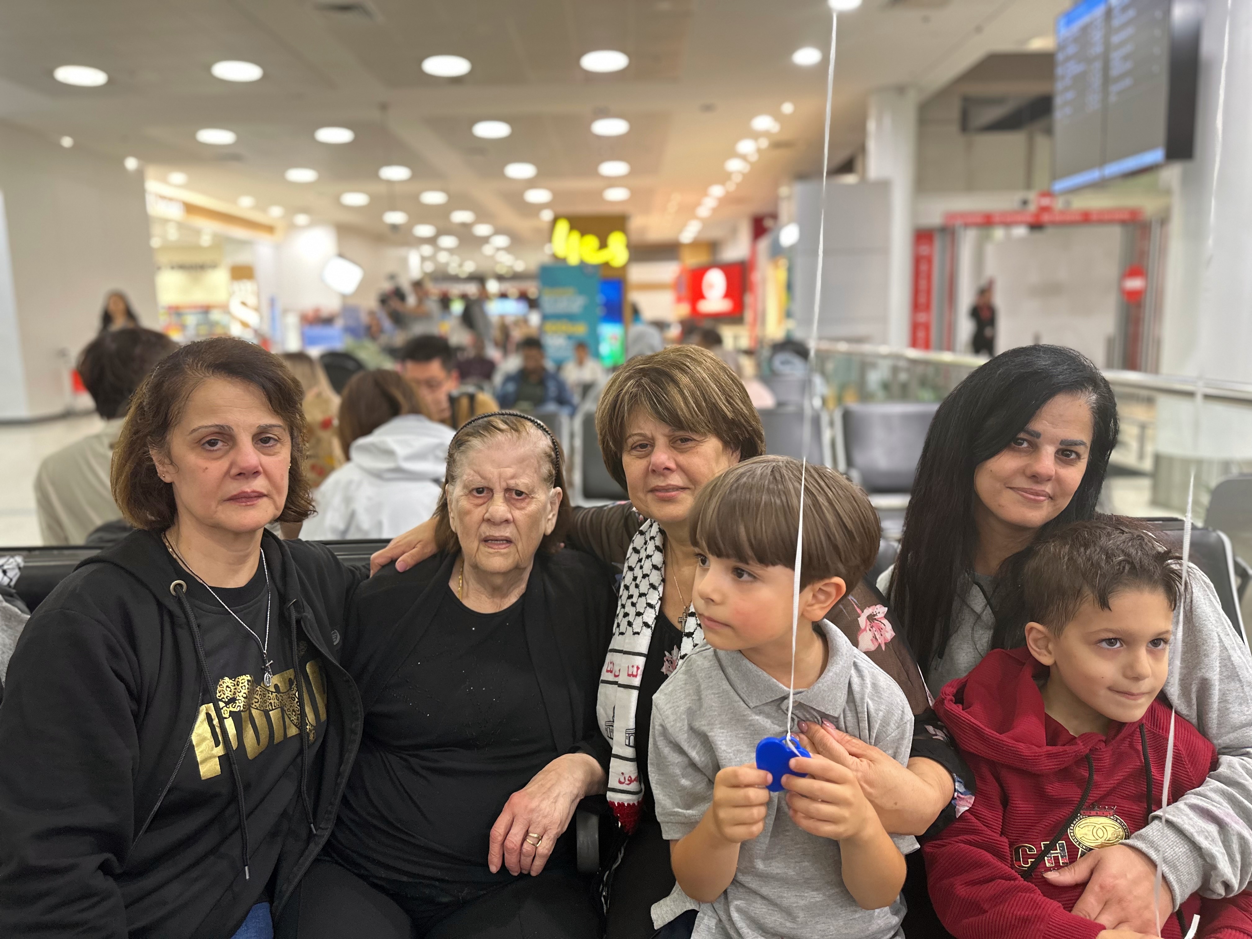 a group women holding two young children sitting at the airport, four of the women are arrivals from gaza