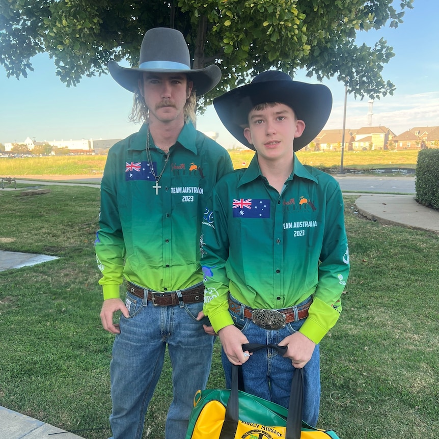 older brother and younger brother stand in park wearing australian rodeo jerseys and cowboy hats