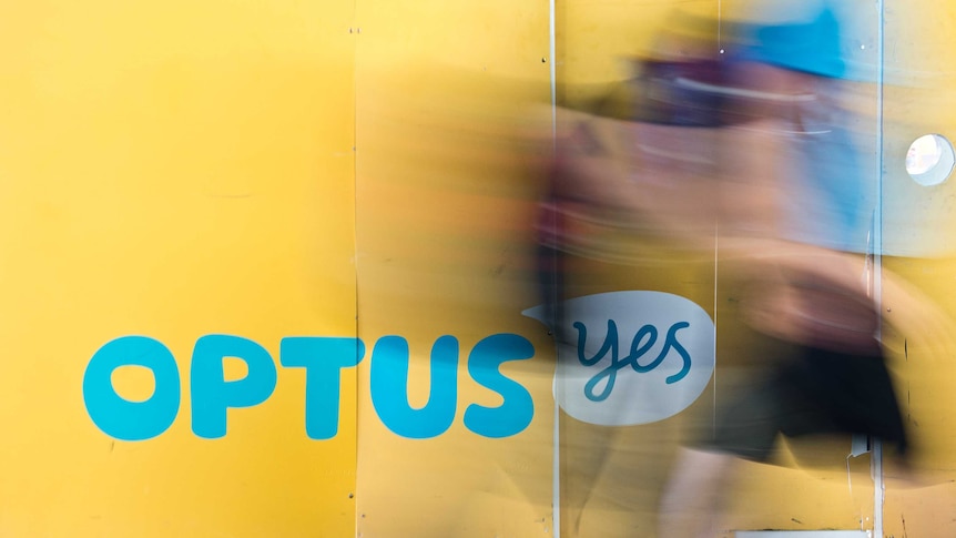 Optus signage on a wall with a blurred image of a person walking past.