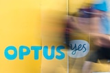 Optus signage on a wall with a blurred image of a person walking past.