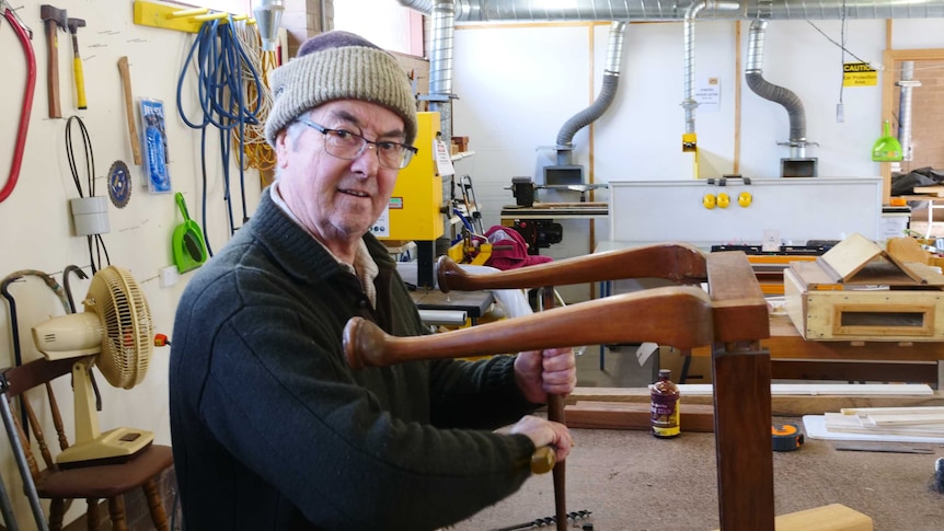 Man poses with tools in the shed as he fixes a wooden chair