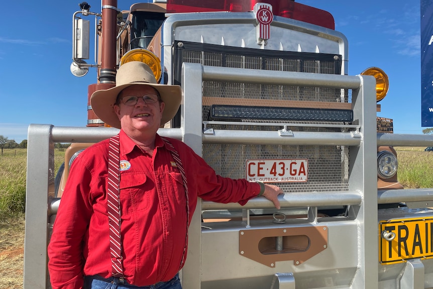 A man in a cowboy hat and bright shirt standing in front of a big rig.