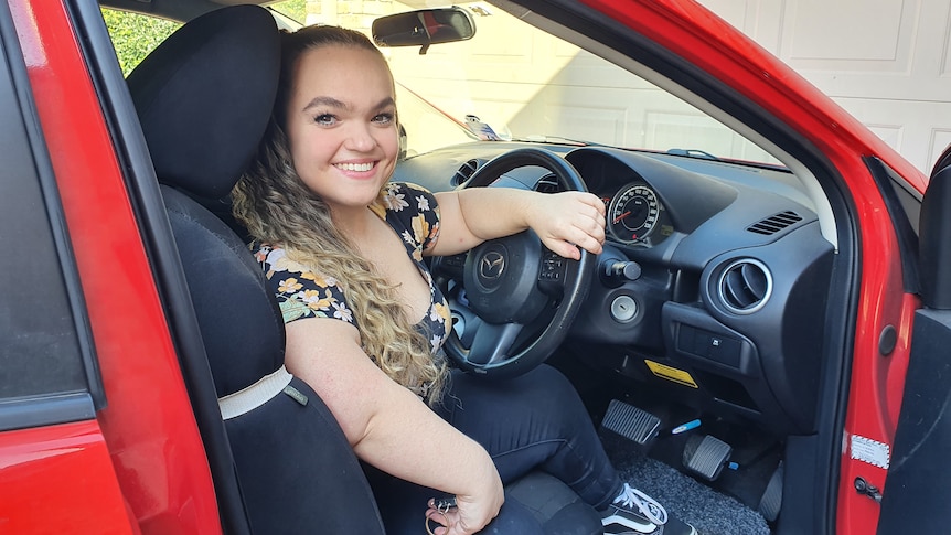 Short-stature woman sitting in the drivers seat of a car with the door open