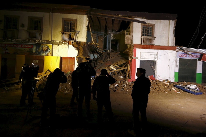 Members of the media gather in front of a damaged building