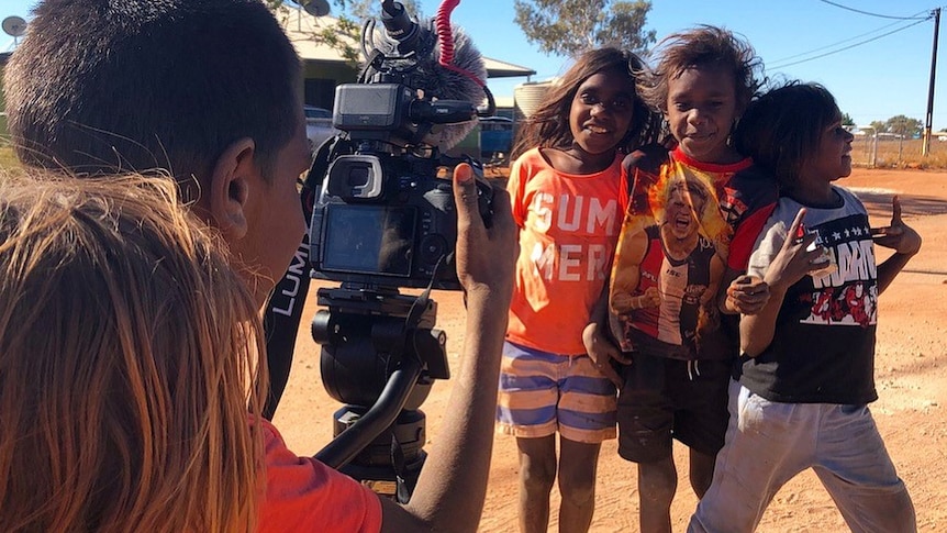 Three Aboriginal children pose for the camera as one of their mates is behind the camera taking the photo