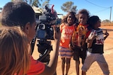 Three Aboriginal children pose for the camera as one of their mates is behind the camera taking the photo