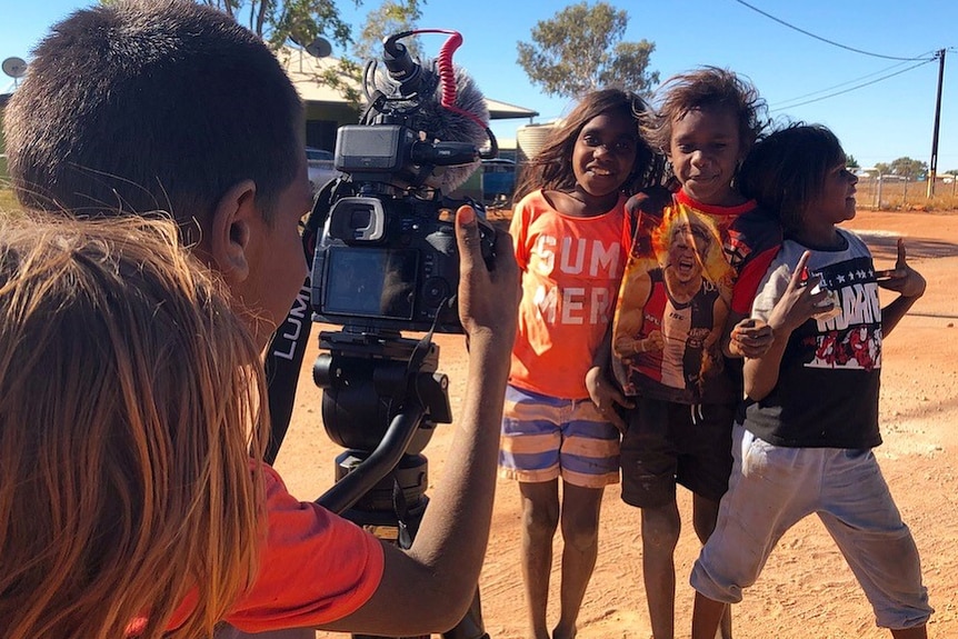 Three Aboriginal children pose for the camera as one of their mates is behind the camera taking the photo.