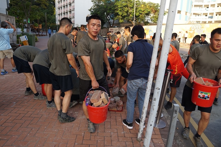 Soldiers carry buckets filled with bricks.