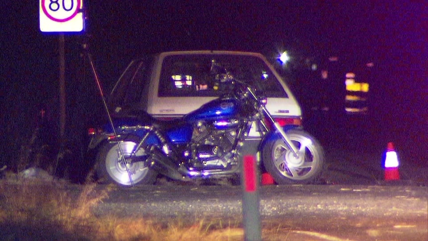 A large motorcycle next to a car and an 80 sign
