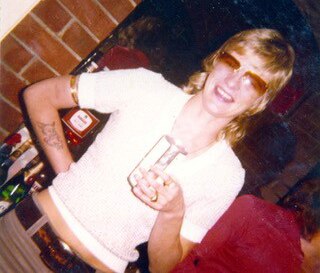 Shirley Finn's former girlfriend Rose Black stands smiling holding a drink in a glass and wearing sunglassses.