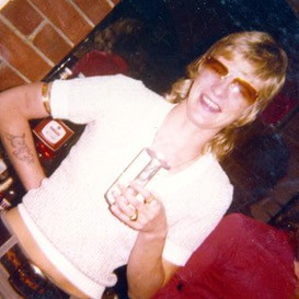 Shirley Finn's former girlfriend Rose Black stands smiling holding a drink in a glass and wearing sunglassses.